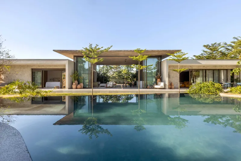 Rear facade reflected in the still pool with planted courtyard trees framing the pavilion