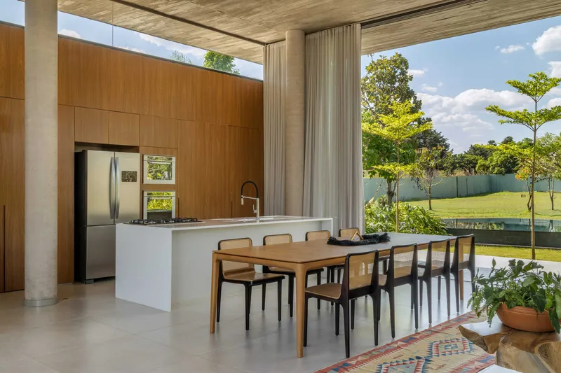 Open kitchen and dining area with timber wall and concrete column framing views to lawn