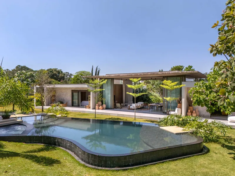Raised pool with curved edges and glass fence facing a low pavilion under mature trees