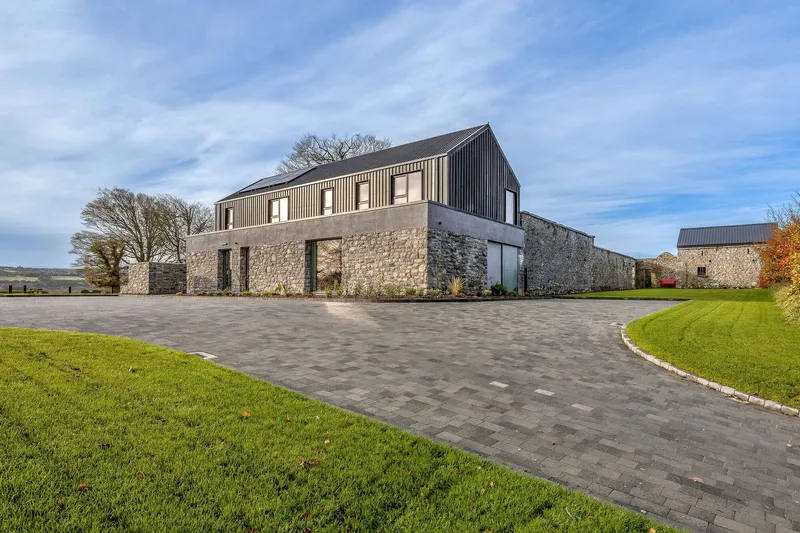Stone base with corrugated metal upper volume viewed across a paved driveway and lawn