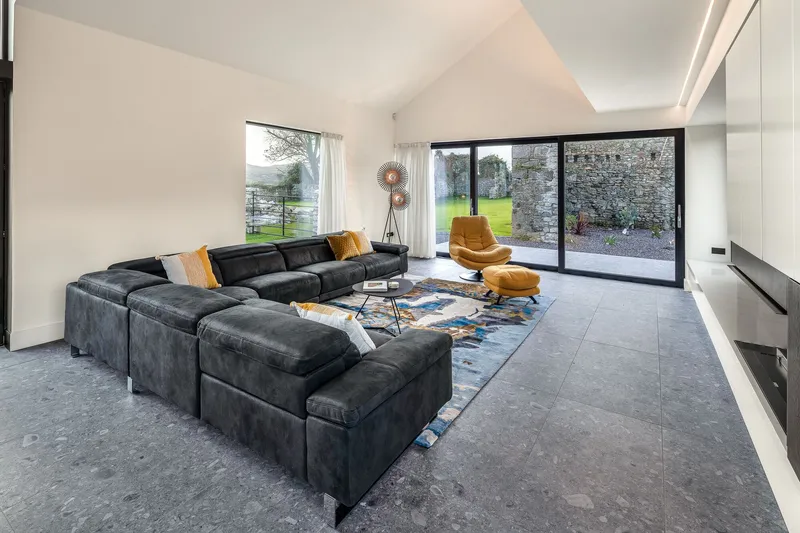 Living room with black modular sofa and floor-to-ceiling glazing overlooking a stone wall