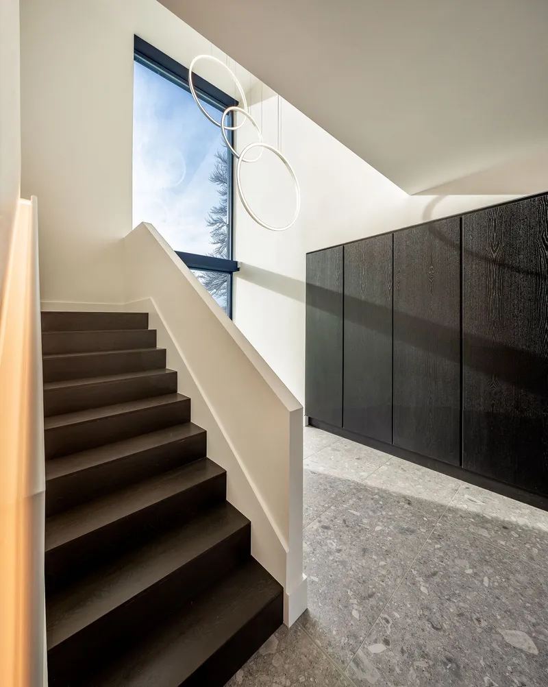 Staircase with white handrail and clerestory window casting afternoon sunlight on dark wood panels