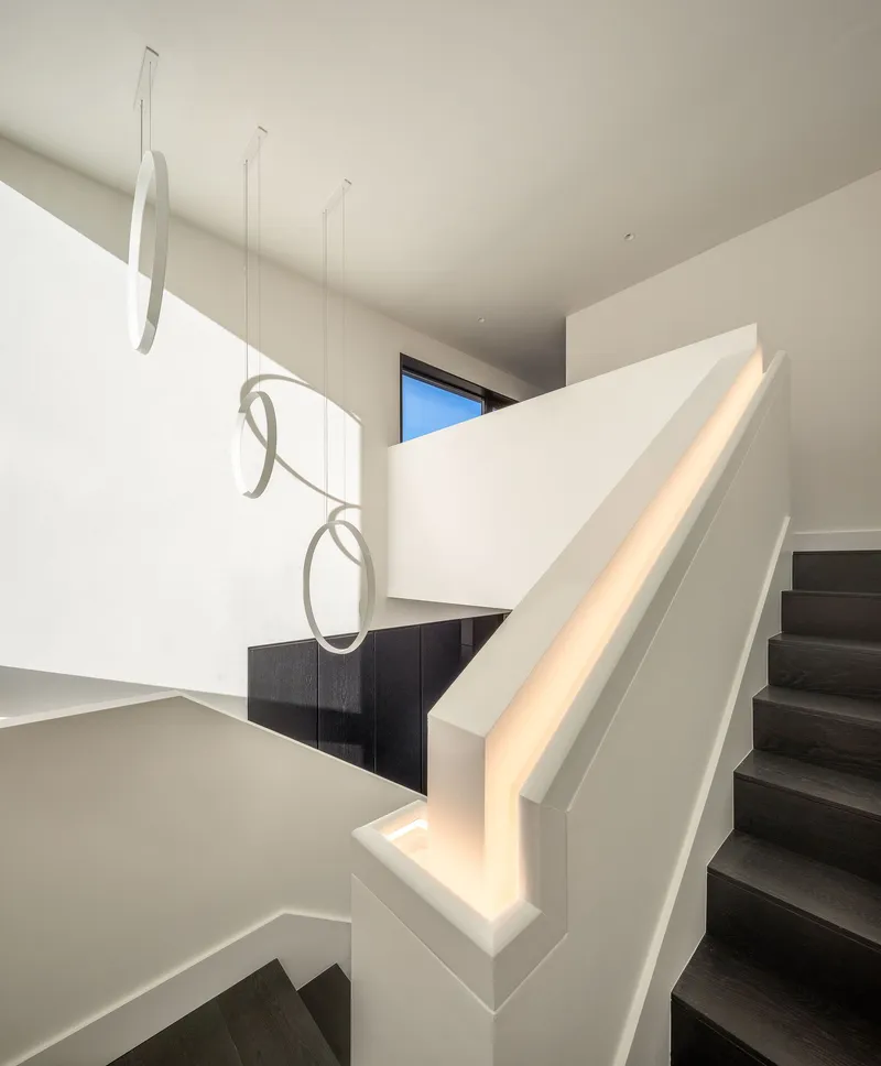 White stairwell with integrated LED handrail and sculptural ribbon pendant fixture suspended in the void