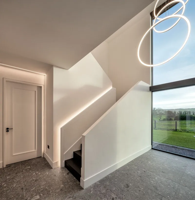 Entry hall showing illuminated stair balustrade and floor-to-ceiling glazing overlooking green fields
