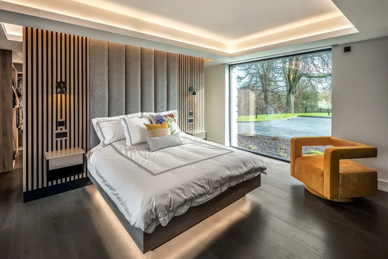 Bedroom with vertical timber slat wall behind upholstered headboard and full-height window facing lawn
