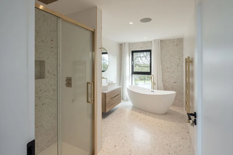 Bathroom with terrazzo flooring, freestanding tub and textured limestone wall panels