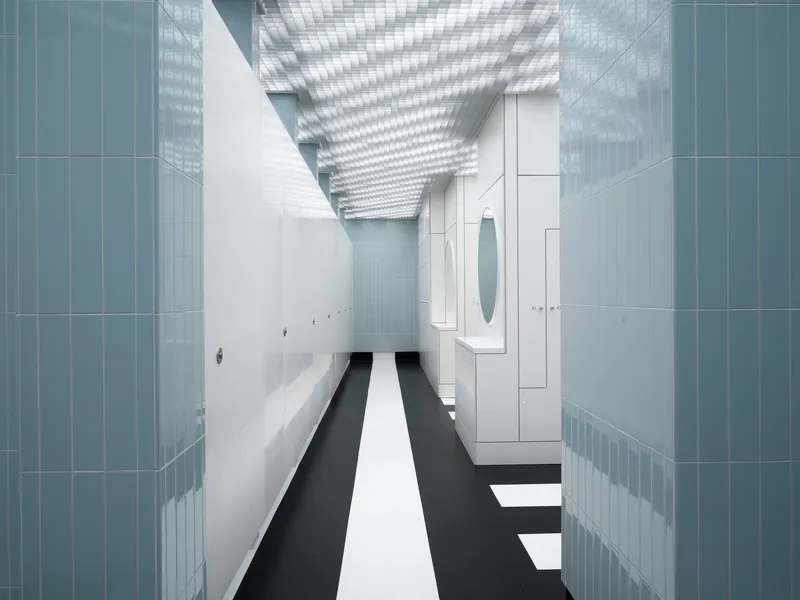 Interior corridor with blue tile walls, black and white striped floor beneath a grid ceiling skylight