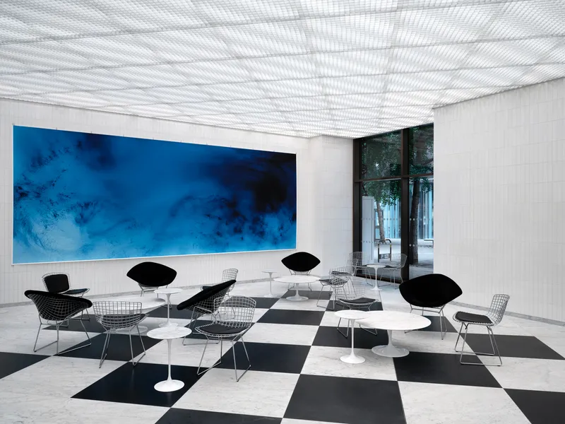 Seating area with wire chairs and round tables beneath a patterned light projection on the ceiling