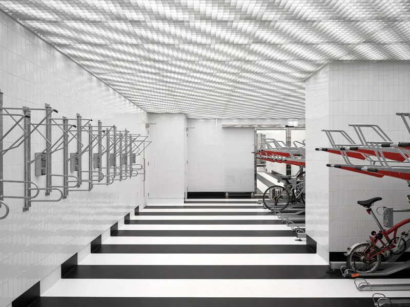 Bicycle storage room with vertical racks and red bikes under a ceiling casting striped shadows