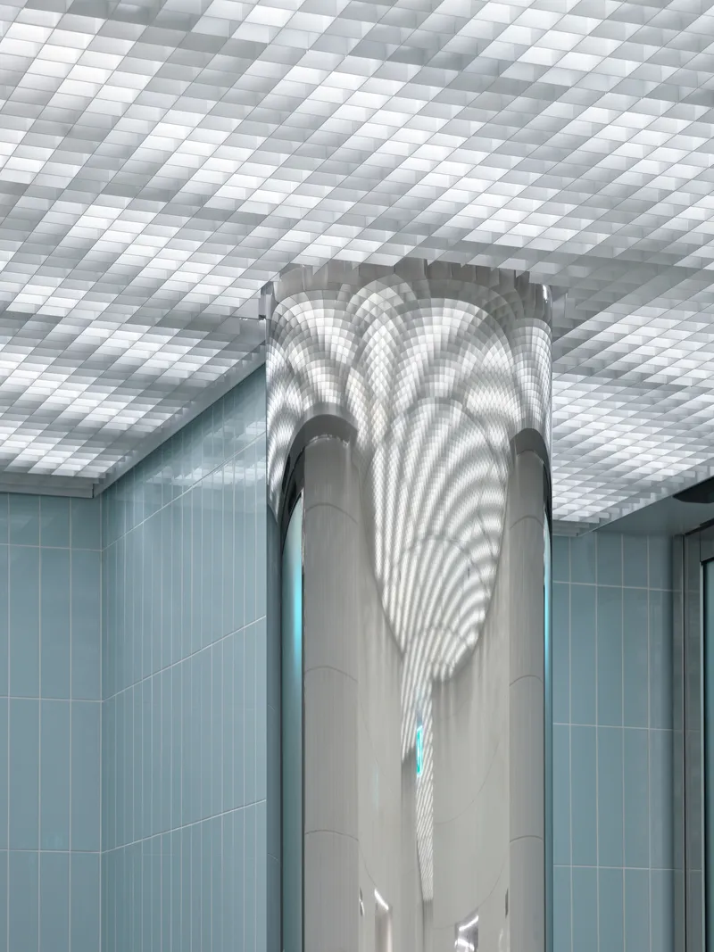 Central column wrapped in smooth paneling beneath a coffered translucent ceiling with light blue tiled walls