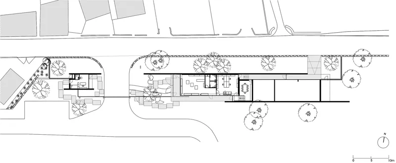 Site plan drawing showing a linear building with curved pathways and trees indicated in the landscape