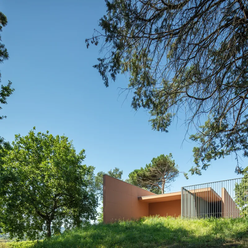 Terracotta walls and vertical metal screening atop a naturalized berm under deciduous and pine trees