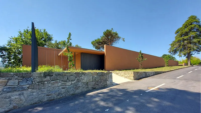 Street view showing the terracotta facade with recessed entry and vertical screening above a stacked stone retaining wall