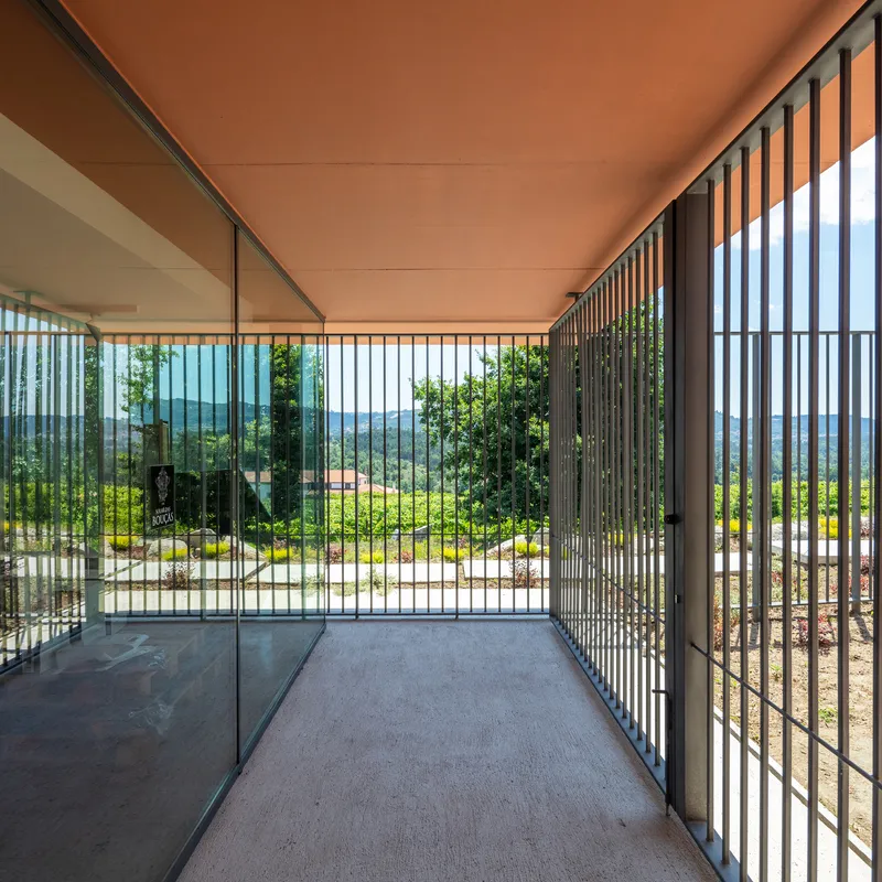 Covered terrace with terracotta soffit, glass walls, vertical metal screens and views toward planted slope beyond
