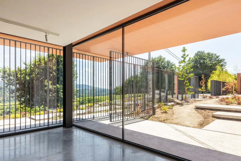Interior room with polished concrete floor opening through sliding glass to a courtyard with vertical metal screens