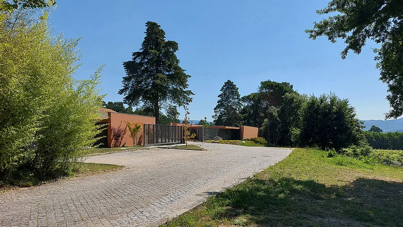 Cobblestone driveway curving toward the low-slung facade with perforated metal screen and tall conifer trees behind
