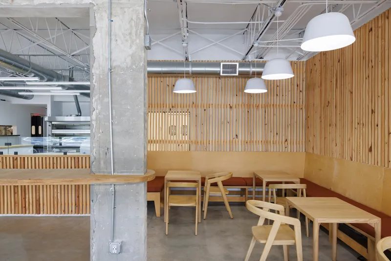 Booth seating with plywood banquette and timber chairs beneath vertical slat wall with backlit opening