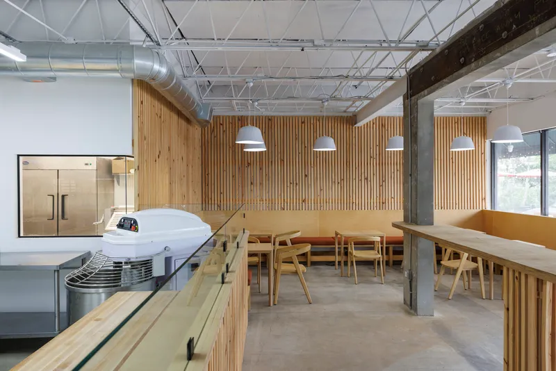 Dining area with timber tables and benches against a vertical slat wall beneath exposed structure