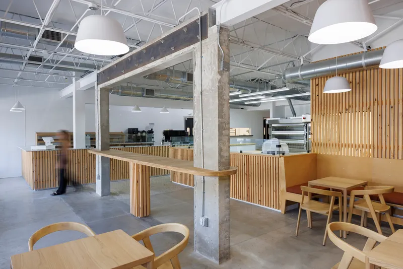 Bakery interior with vertical timber slat counters and exposed concrete columns beneath white pendant lights