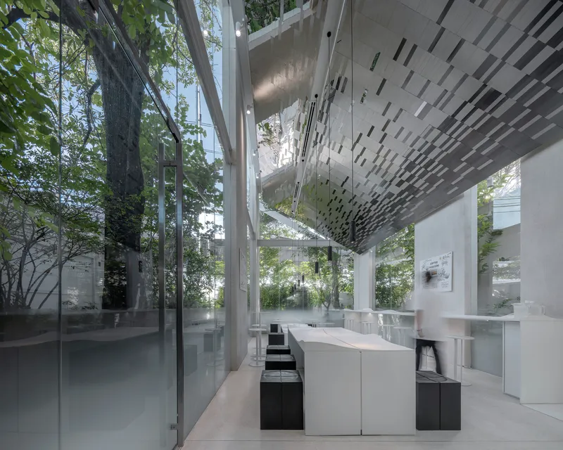 White service counter beneath perforated ceiling panel with full-height glazing framing trees outside
