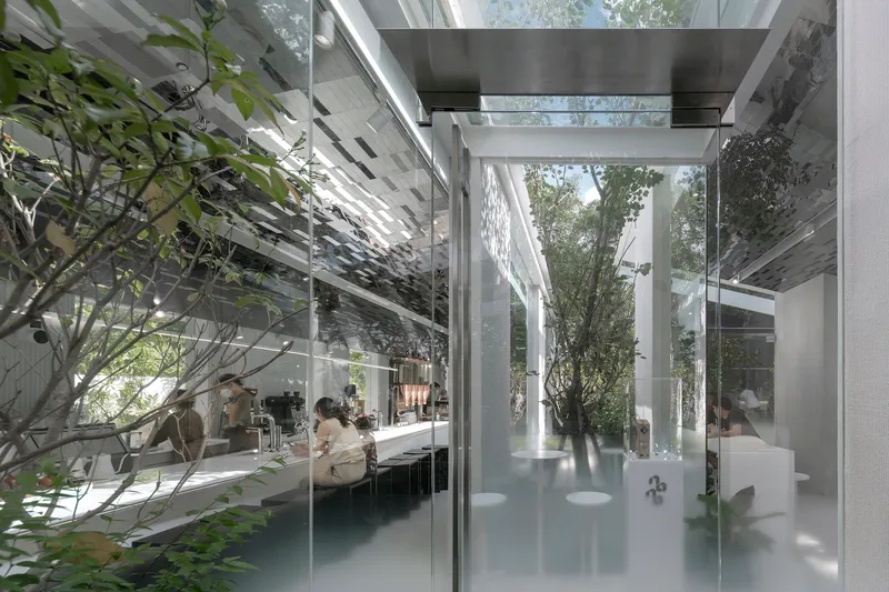 Glass-enclosed interior courtyard with trees and visitors at long white tables beneath a pixelated ceiling