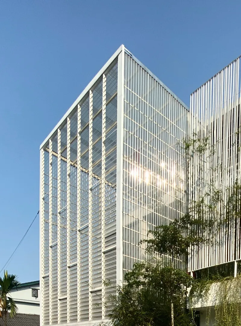 White vertical louver facade with horizontal brise-soleil framing under clear blue sky with adjacent bamboo plantings