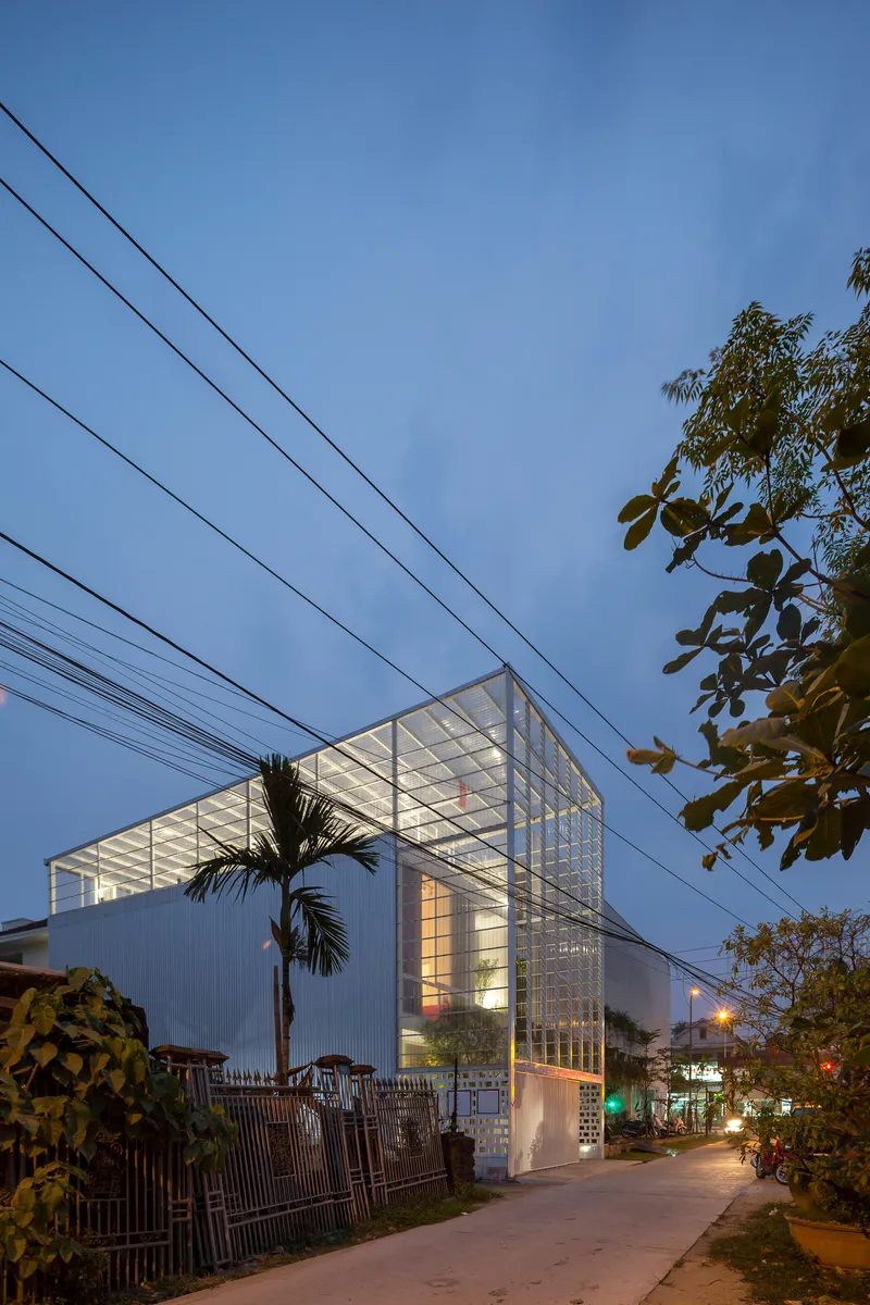 Street view of the glass-enclosed upper volume cantilevering above white louvers at dusk with overhead power lines