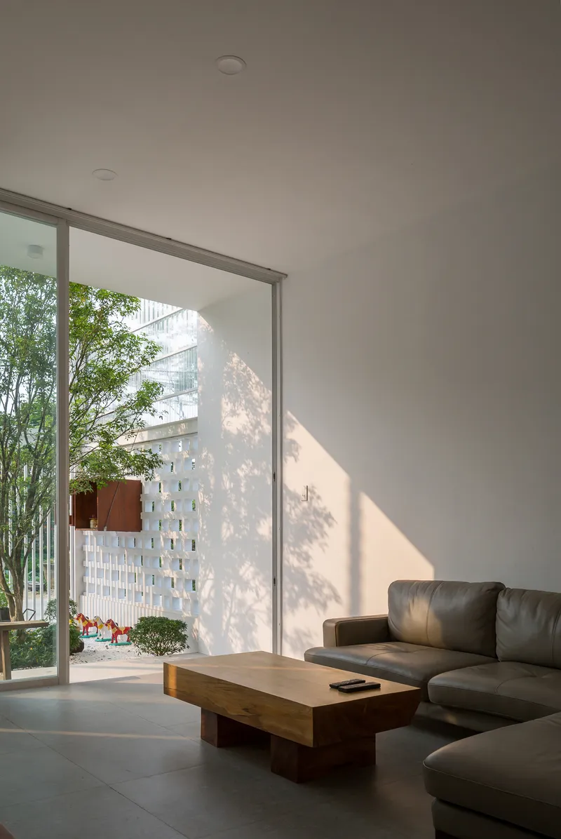 Living room with floor-to-ceiling glazing overlooking a courtyard with bamboo and perforated white screen wall