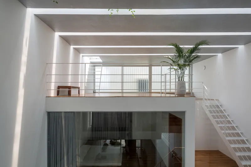 Double-height interior space with mezzanine bridge, white tube steel railing, and recessed ceiling skylights