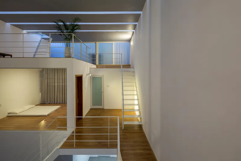 Interior view of the split-level volume with white metal railings and timber staircases under skylights