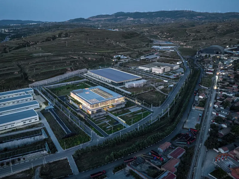 Drone view of the illuminated building surrounded by industrial structures and agricultural terraces at twilight
