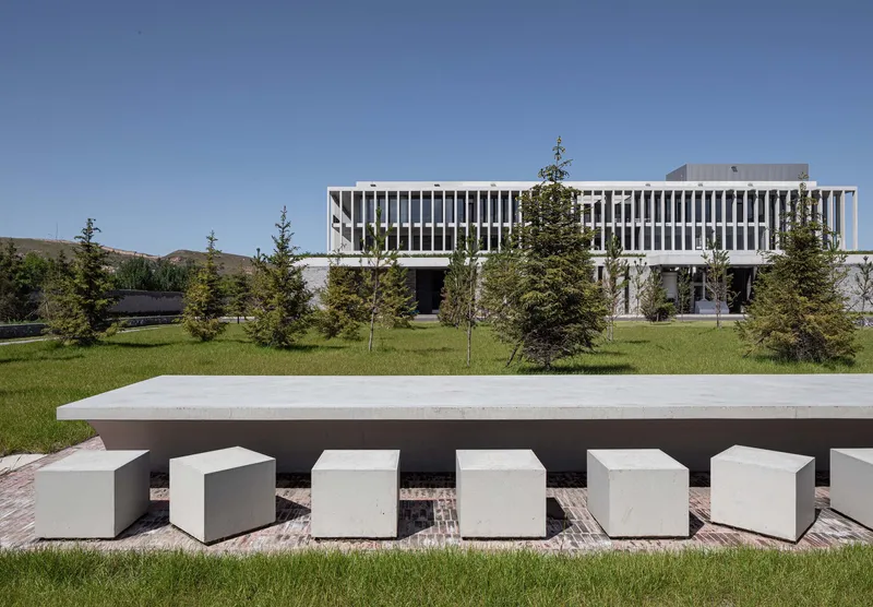 Outdoor seating area with concrete table and cube stools on a lawn before the vertical-louvered facade