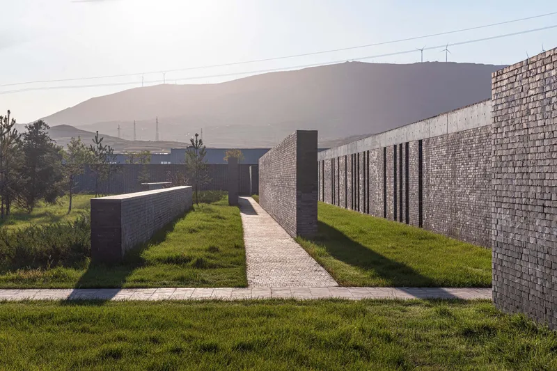 Concrete pathway between low masonry walls leading toward a hillside at dusk