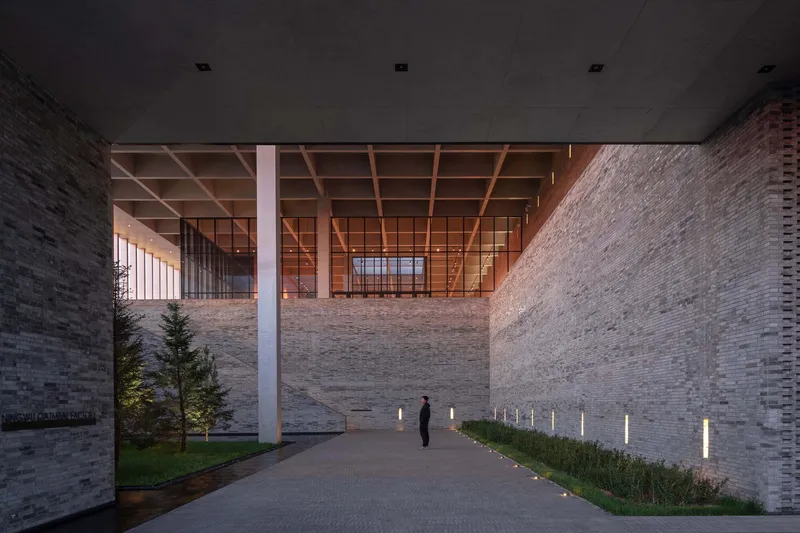 Covered entrance passage with timber coffered ceiling and a figure walking between masonry walls at twilight