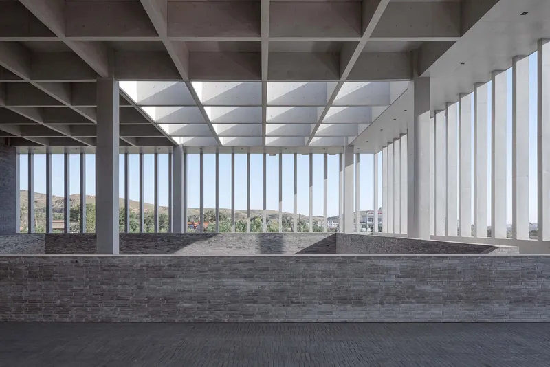 Interior hall with coffered concrete ceiling and vertical fin windows overlooking distant hills