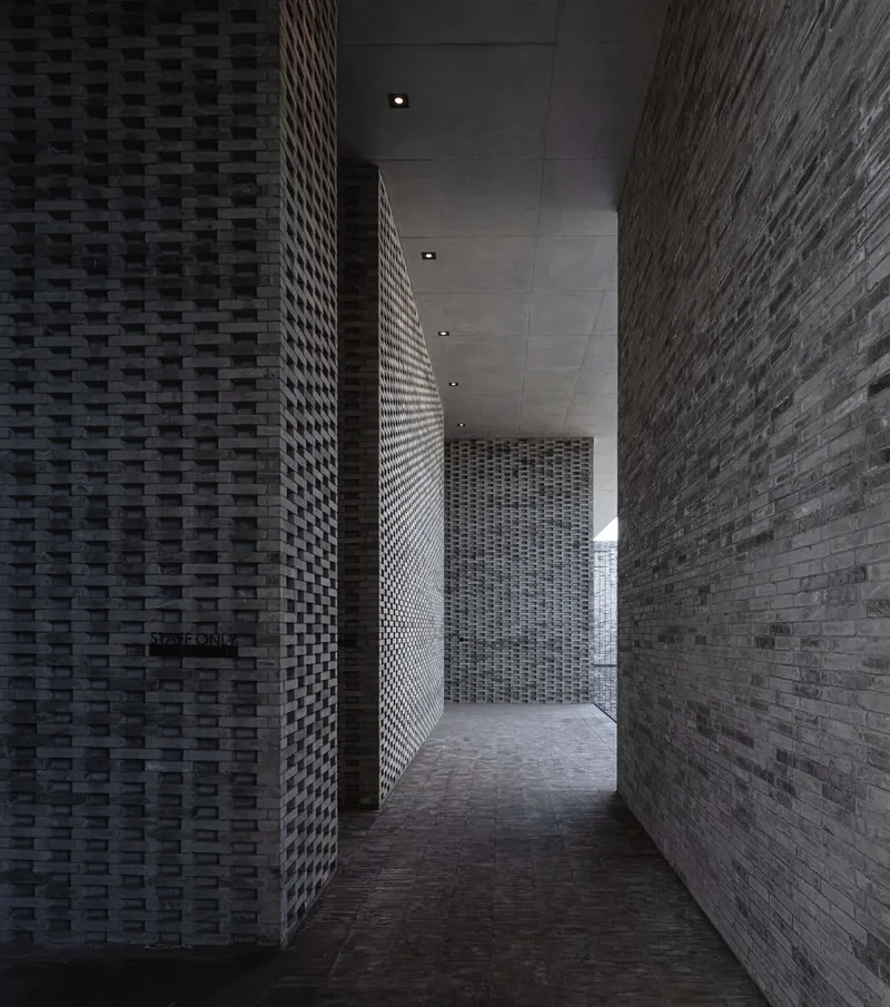 Narrow corridor with basketweave brick walls and recessed ceiling lights leading deeper into the space