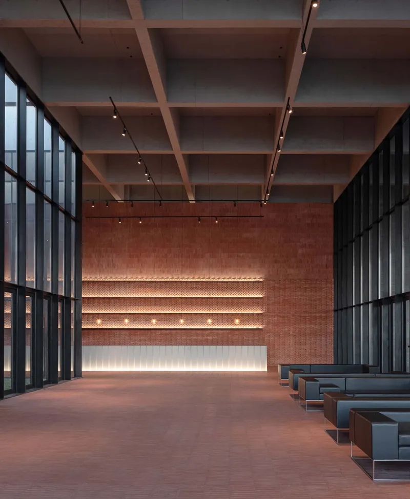 Timber coffered ceiling above a lobby with illuminated perforated brick wall and steel frame glazing
