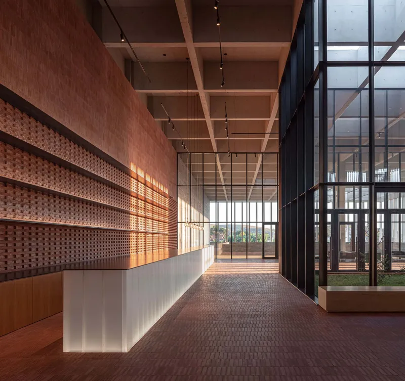 Long corridor with perforated brick wall and timber beams alongside floor-to-ceiling steel windows