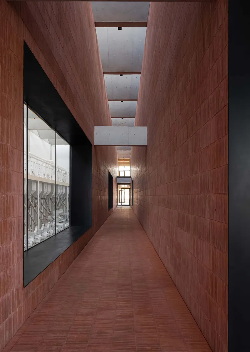 Narrow hallway clad in reddish timber panels with concrete ceiling beams and glazed display case