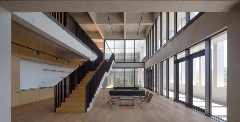 Double-height lobby with timber staircase, concrete coffered ceiling and floor-to-ceiling glazing overlooking trees