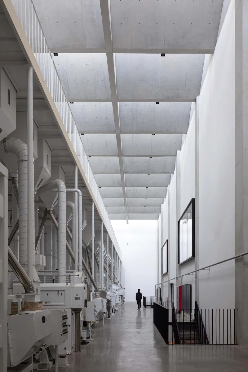 Industrial gallery with exposed white mechanical ducts along one wall and coffered concrete ceiling overhead