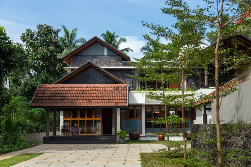 Layered gabled roofs with clay tile and corrugated metal set among palm trees and lush vegetation