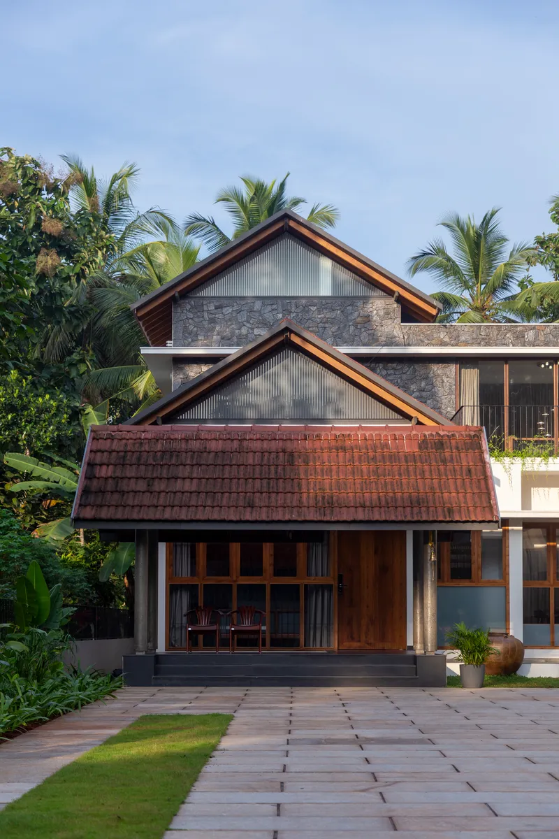 Front facade showing stacked gabled forms with stone and metal cladding against palm trees