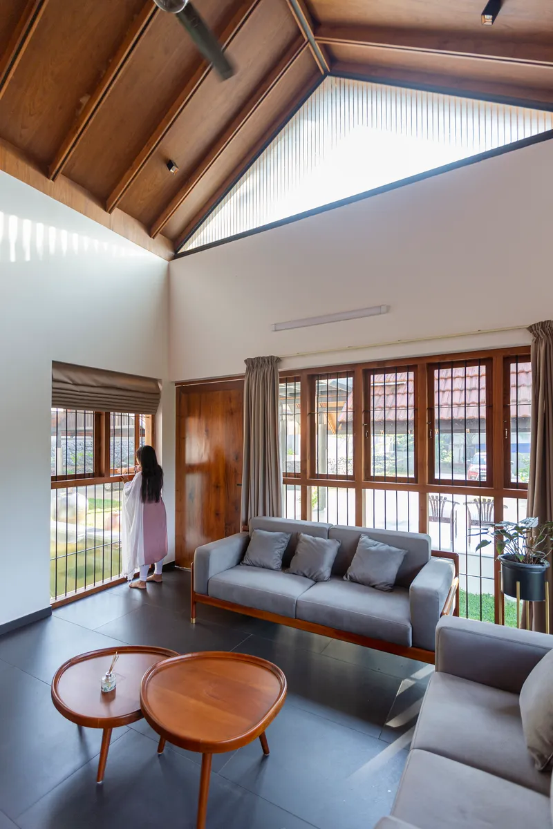 Double-height living room with exposed timber rafters, wood-framed windows and a woman looking outside