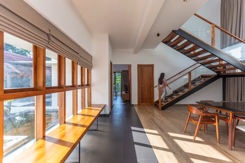 Interior hallway with open-tread timber staircase and continuous wood-framed glazing casting afternoon sunlight