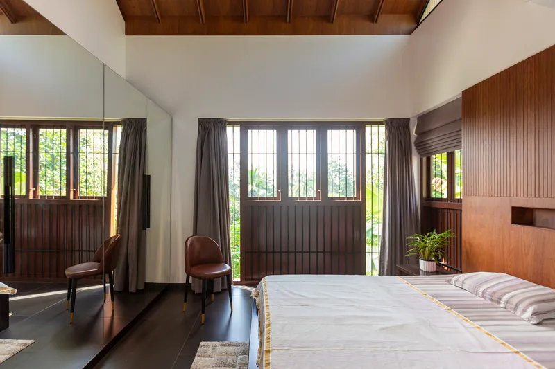Bedroom with wood-paneled gabled ceiling and gridded windows framing the garden beyond