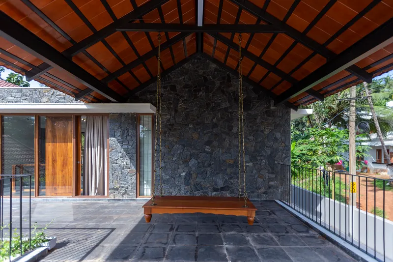 Covered terrace with exposed timber roof structure, dark stone wall and a suspended wooden swing