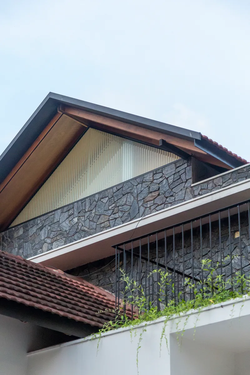 Upper level facade with corrugated metal gable panel, stone balcony parapet, and planters below a cloudy sky