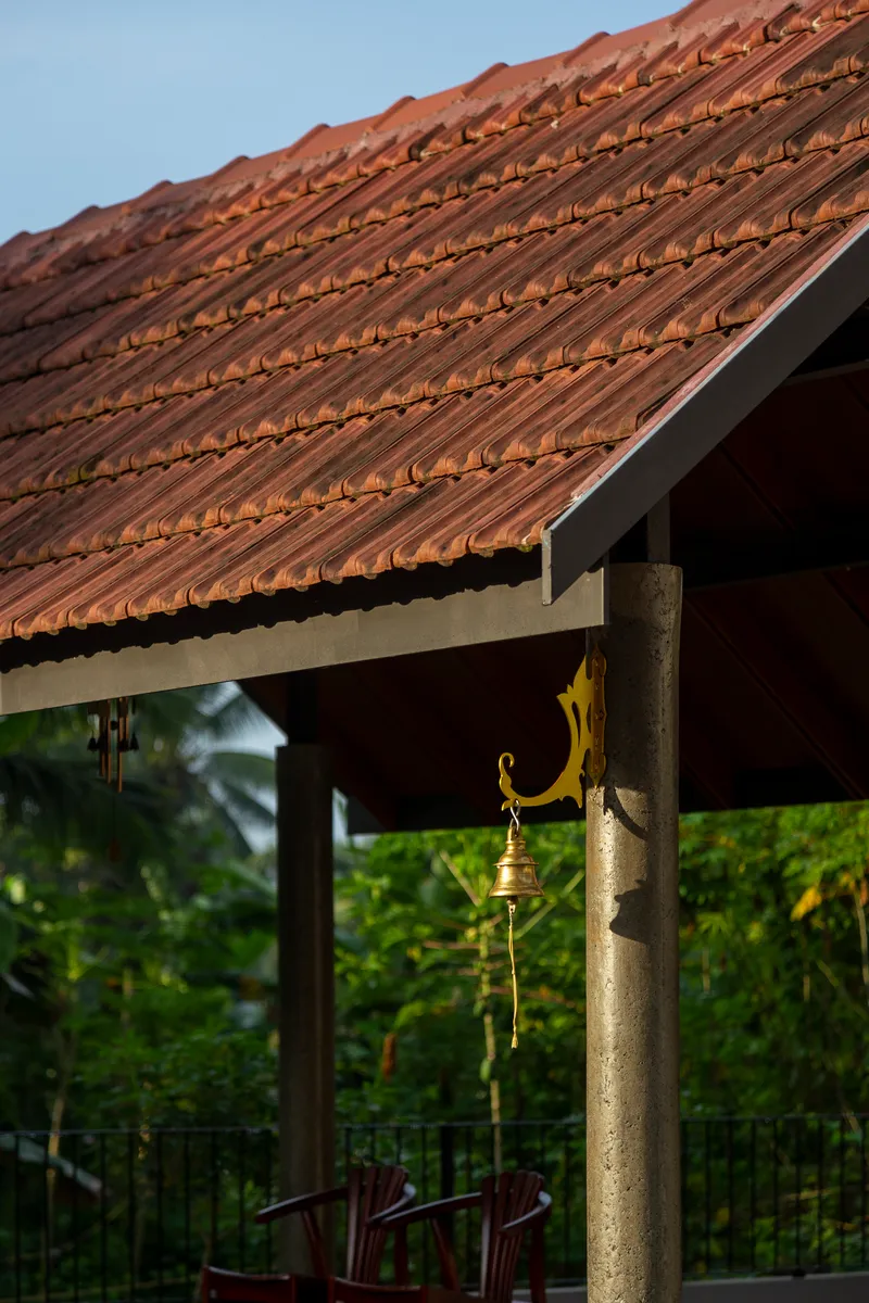 Close-up of clay tile roof overhang with exposed eaves above a covered porch and brass bell