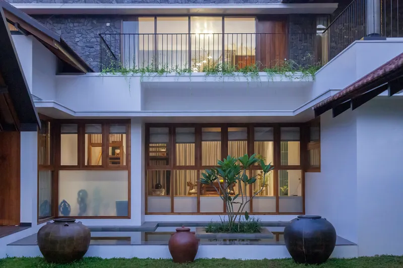 Interior courtyard view with timber-framed glazing, planted terrace above, and ceramic urns at dusk